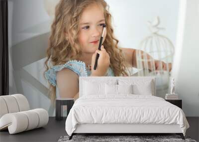 Cute little girl applying make up looking into mirror. Little fashionista girl playing with her mother`s cosmetics. Adorable child indoors Wall mural